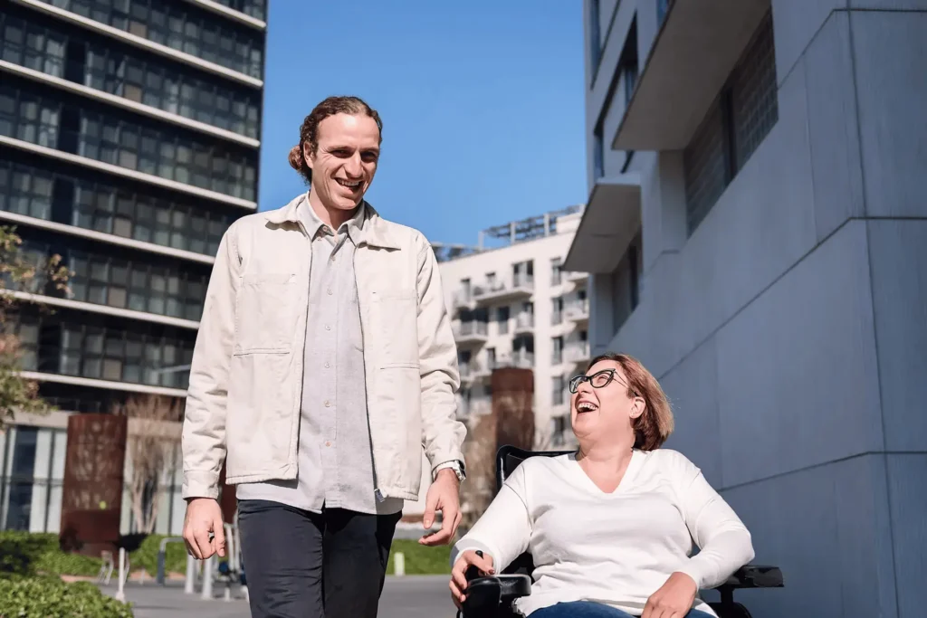 Two people smiling and talking, one using a wheelchair.
