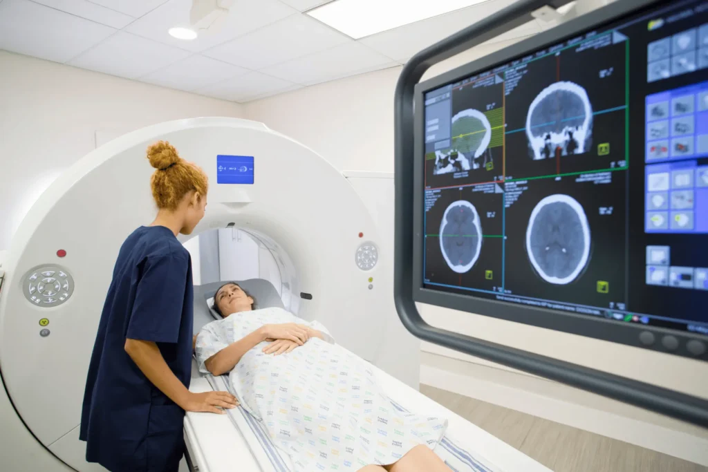 Patient undergoing a CT scan while a healthcare worker reviews brain images.