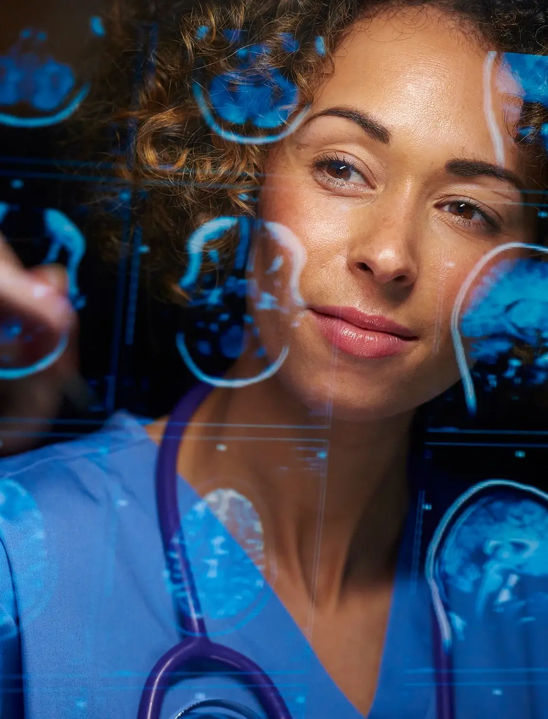A female doctor in blue scrubs and a stethoscope looks at brain scan images displayed on a transparent screen, appearing focused and thoughtful.
