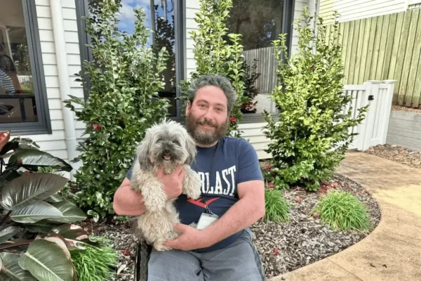 Man in a wheelchair holding a dog outdoors and smiling.