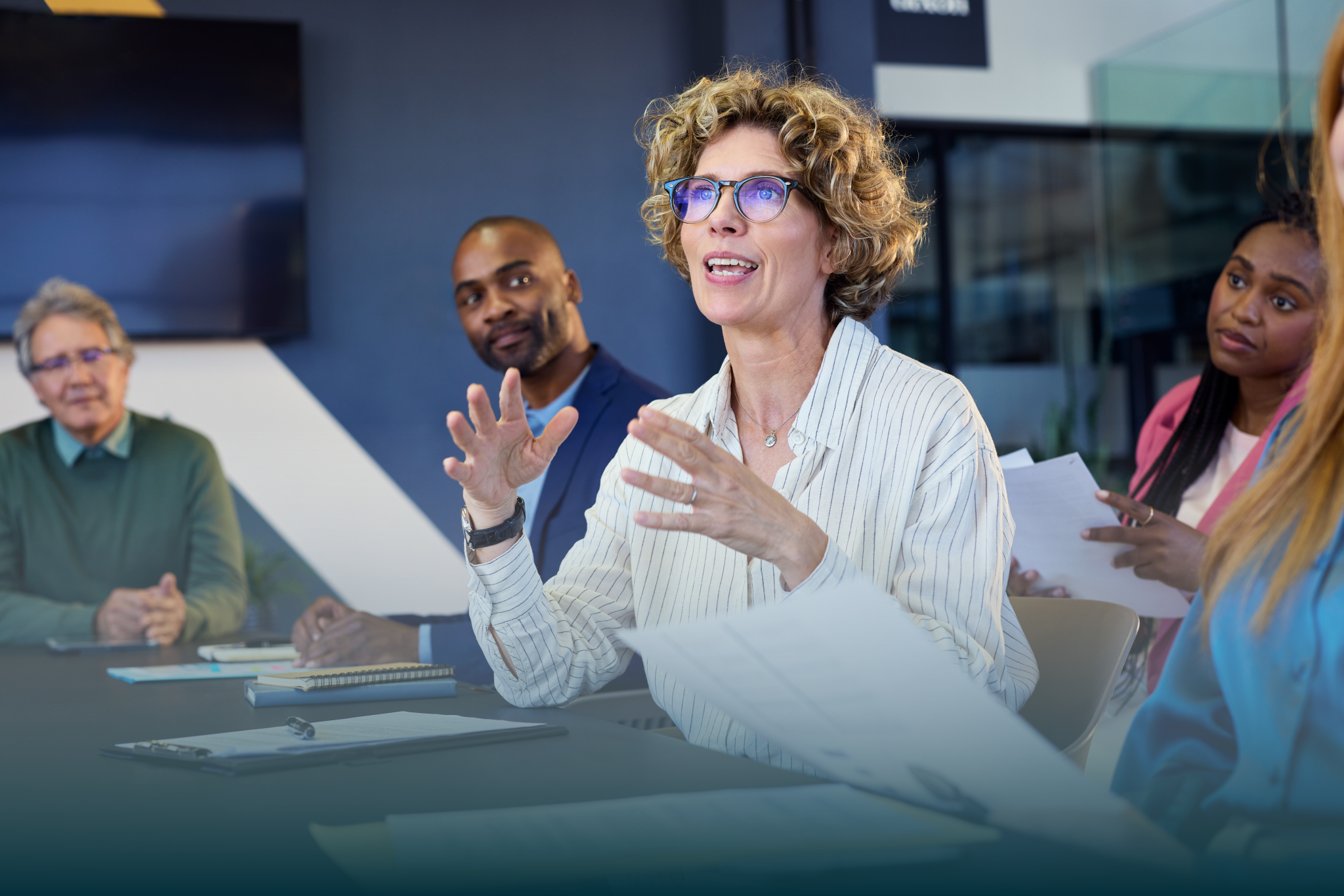 Mature business female manager guiding employees in meeting. Group of businessman and businesswoman working together while brainstorming and sharing new ideas and strategy. Portrait of female leadership explaining report to multiethnic business group, discussing work in conference room.